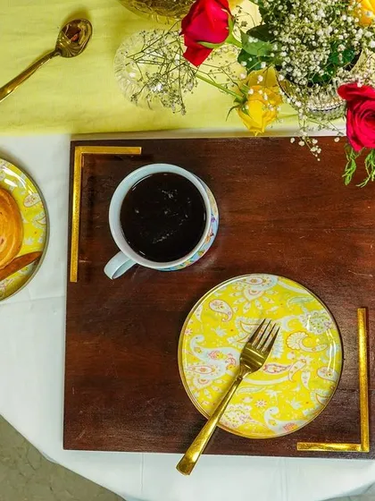 A top-down view of a breakfast-in-bed tray, featuring bright yellow patterned plates and golden cutlery.