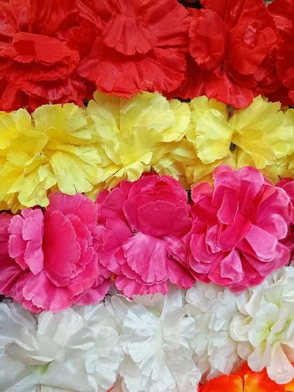 A handful of colorful artificial carnation flower strings. These are available in various colors like red, yellow, pink, and white, and are perfect for creating garlands or decorating frames.