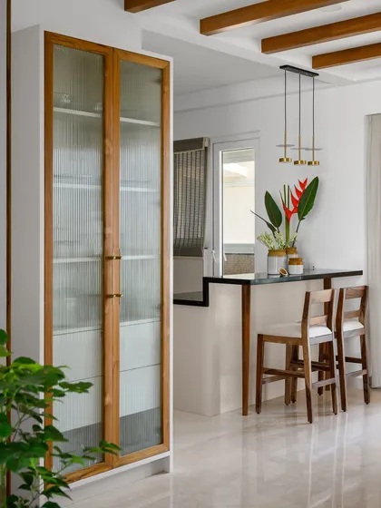 This dining space in 'Malhar' is adorned with a full-height crockery unit featuring fluted glass doors, providing elegant storage that complements the adjacent breakfast counter.