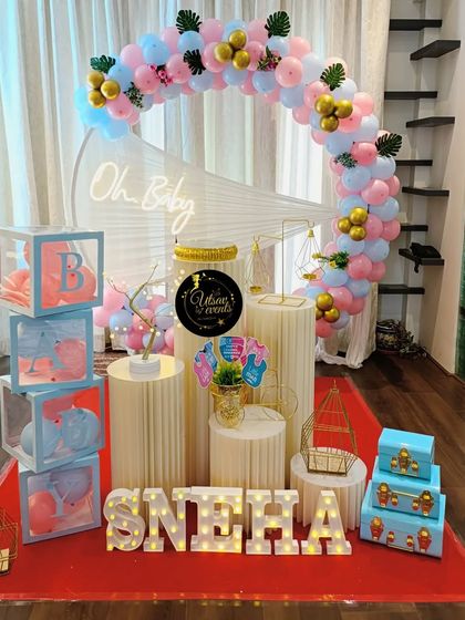 A modern 'Oh Baby' shower theme with pastel pink and blue balloons. The decor includes a neon sign, transparent 'BABY' blocks, and marquee letters for the name.