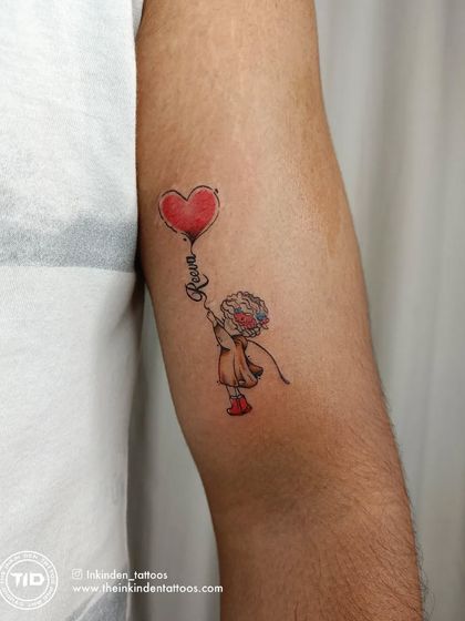 A father's love for his daughter, captured in a charming watercolor-style tattoo. The design shows a little girl holding a heart-shaped balloon with her name, "Reeva," written in the string.