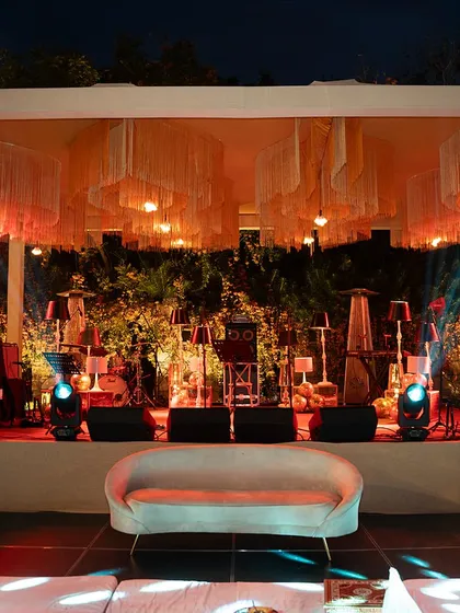 The stage for a sangeet night, featuring a backdrop of vintage lamps and fringed chandeliers. This setup was designed to create a warm, intimate, and slightly retro atmosphere for the evening's performances.