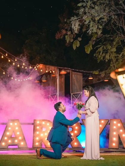 A romantic proposal captured from a creative angle, framed by glowing street lamps. The dramatic smoke and lighting add a touch of magic to this important life event.