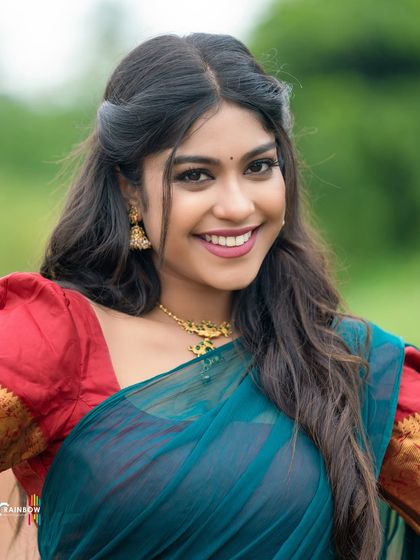 A happy and candid shot of a model in a teal and red half saree, showcasing her natural smile and the outfit's vibrant colors.