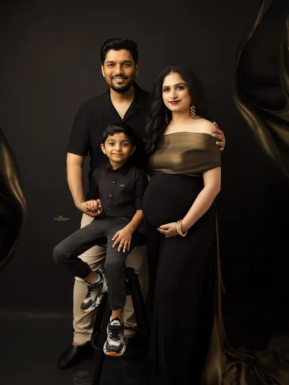 A chic and modern family portrait. Dressed in elegant black and gold, this family of three (soon to be four) poses against a dark backdrop for a sophisticated, high-fashion look.