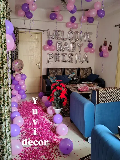 A "Welcome Baby Prisha" room decoration using purple and pink balloons, with a flower petal carpet leading the way.