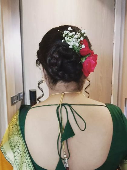 A soft, messy bun woven with fresh red roses and baby's breath. The loose tendrils add a touch of romance, making it a great option for an engagement or reception look.