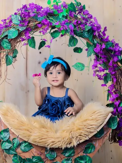 This little girl in a blue dress is playing with a flower, captured in a moment of sweet curiosity during her studio session.