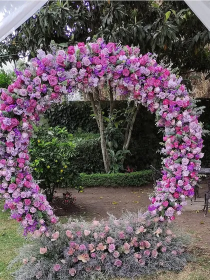 This stunning full-circle floral arch, made with shades of pink and purple roses, creates a breathtaking photo opportunity for any outdoor event.