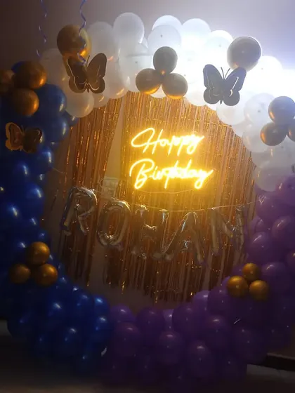 A birthday ring decoration in blue, purple, and white, with gold accents and butterfly stickers. The setup also includes the name "Rohan" in foil balloons.