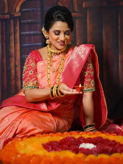 A woman dressed for Diwali, seated by a beautiful flower rangoli and holding a lit diya, surrounded by the warm festive glow.