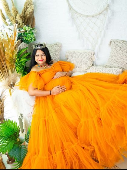 This bright orange tulle gown makes a bold and cheerful statement. The wide shot showcases the full expanse of the dress amidst our indoor studio's botanical and boho elements.