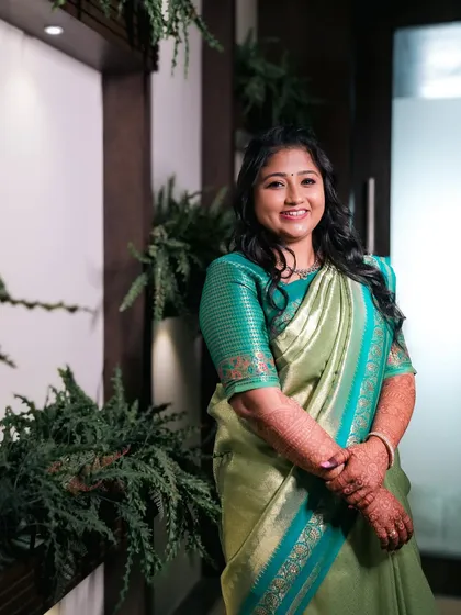A smiling bride in a light green saree, posing for a portrait.