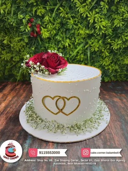 An elegant anniversary cake with two intertwined golden hearts and a fresh red rose on top. A simple and beautiful symbol of your love.