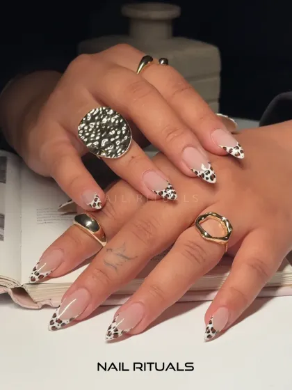 A stylish and trendy nude manicure taken to the next level. This image shows off the glossy finish of our cow print French tips, paired with chunky gold rings.