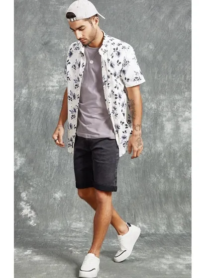 A casual summer look for a men's fashion brand. A floral print shirt is layered over a simple tee with denim shorts, creating an easy, stylish outfit for everyday wear.