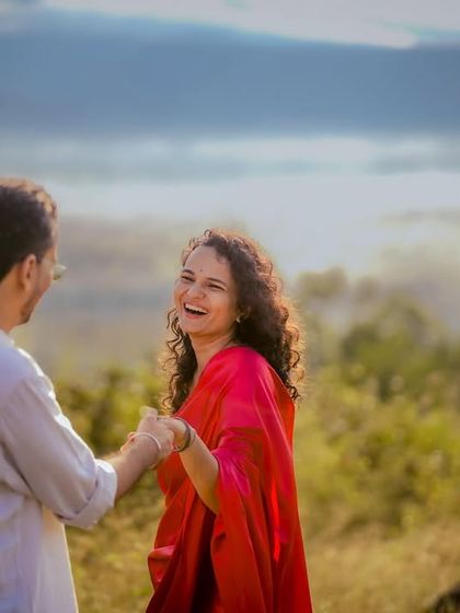 A candid photo filled with laughter as a couple enjoys a moment in a sunlit field, with misty hills in the distance.
