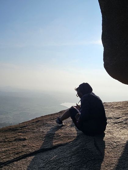 A trekker sits on the rocky slope of Uttari Betta, enjoying the peaceful morning view.