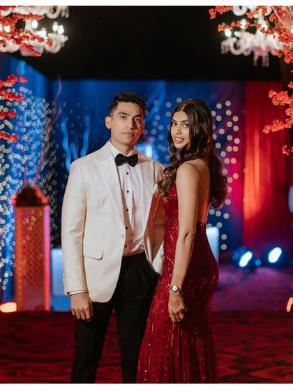 The couple looking sharp and glamorous at their reception party, posing at the entrance of a stunning red-themed decor tunnel.