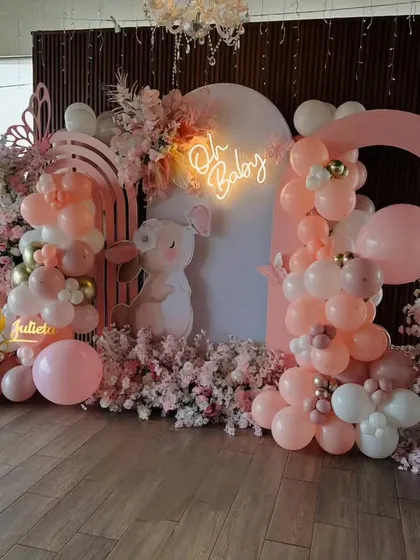 A breathtaking cherry blossom-themed baby shower in shades of pink. This luxurious setup includes an "Oh Baby" neon sign, "BABY" blocks, and is overflowing with pink balloons and faux cherry blossoms.