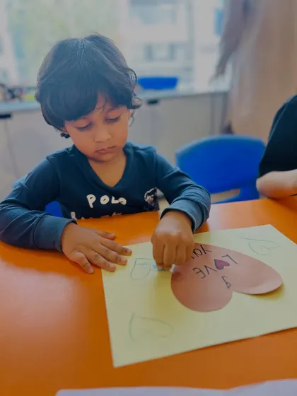 Art and drama go hand-in-hand. A student is carefully crafting a "I Love You" card, an activity that combines fine motor skills with expressing emotion, a core theme of our classes.