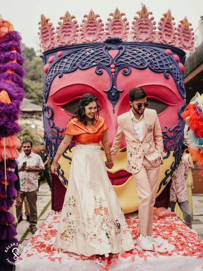 The couple makes a grand entrance at their carnival-themed party, with a huge, colorful mask as a backdrop.