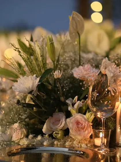 A candlelit dinner setting in Kasauli. The mirrored table reflects the floral centerpiece and the wine glasses, creating a dreamy, layered effect.
