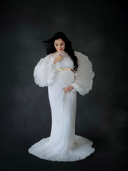 A stunning portrait of a mother-to-be in a unique pleated white gown, creating an angelic and high-fashion look.