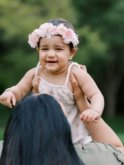 A beautiful outdoor shot of the baby girl at her first birthday, lifted up by her mother, smiling and happy.