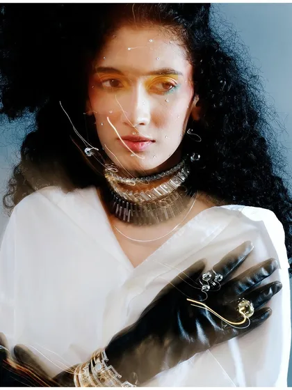 An experimental portrait using a slow shutter speed and light streaks to create a fractured, energetic effect. The styling with leather gloves and layered jewelry adds to the edgy, high-fashion feel.