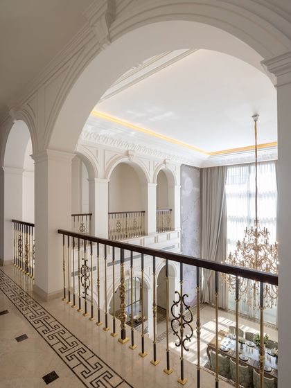In The Ivory Royale, corridors are designed to carry character and a sense of rich silence. This view from the upper gallery looks down into the double-height dining area, framed by a series of grand neoclassical arches and ornate railings.