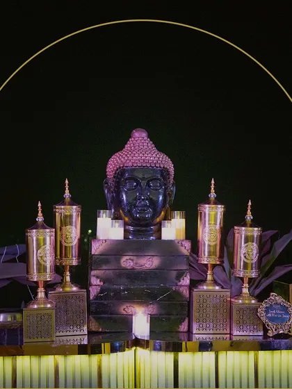 A serene and opulent setup featuring a Buddha statue as the centerpiece, surrounded by ornate golden urns and candlelight, creating a tranquil yet luxurious focal point.