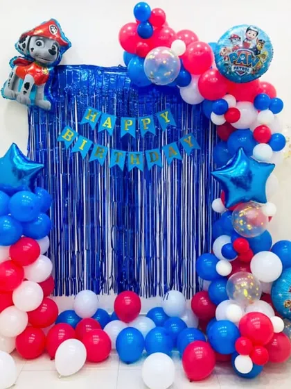 A simple yet fun Paw Patrol birthday decoration for a home celebration. This setup features a blue foil curtain backdrop, a 'Happy Birthday' banner, and a balloon frame in the theme's signature red, blue, and white colors.