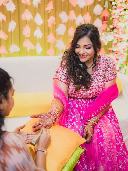 A sweet moment during the Mehendi application. The bride's pink lehenga and soft makeup create a look of youthful charm.
