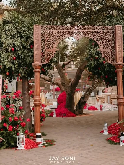 I created an entrance that blends tradition with nature for this Mehfil-e-Mehendi. A beautifully carved wooden archway, surrounded by lush trees and vibrant red floral arrangements, sets a warm and inviting tone.