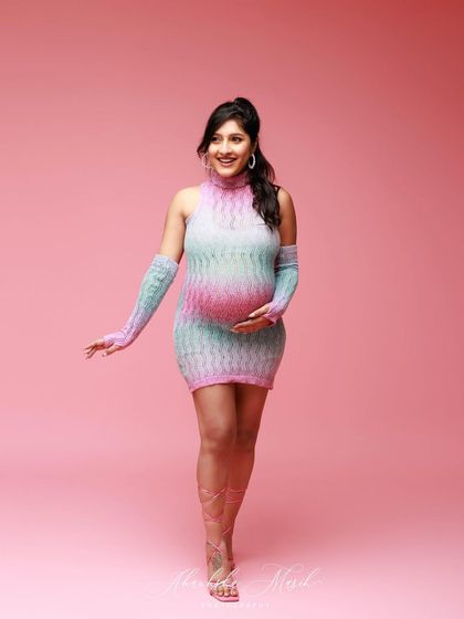 A fun and modern maternity look with a colorful knit dress and matching gloves, set against a vibrant pink backdrop for a playful feel.
