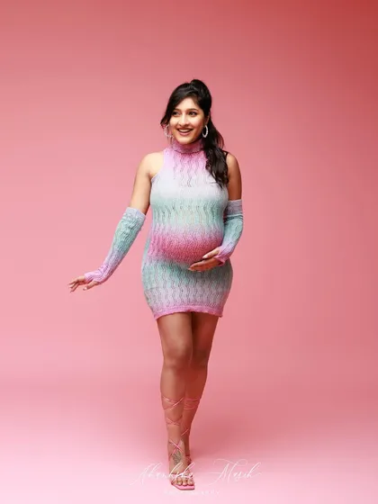 A fun and modern maternity look with a colorful knit dress and matching gloves, set against a vibrant pink backdrop for a playful feel.