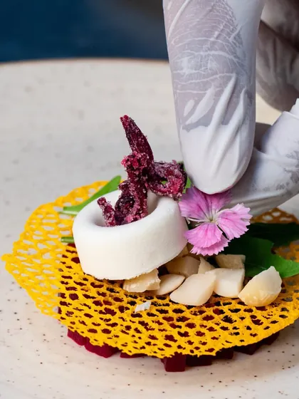 A chef meticulously places an edible flower on a deconstructed berry pudding with an almond tuile. This image highlights the artistry and precision that goes into our gourmet dessert plating.