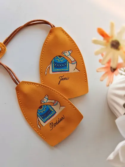 A pair of mustard yellow leather keychains, each featuring a hand painted camel and personalized with the names 'Tani' and 'Poddar'. The warm colors and artistic touch make these truly special.