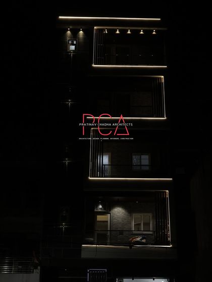 A subtle night photograph of 'The Cursive Abode', focusing on the quiet elegance of the illuminated balconies and the dark, textured facade.