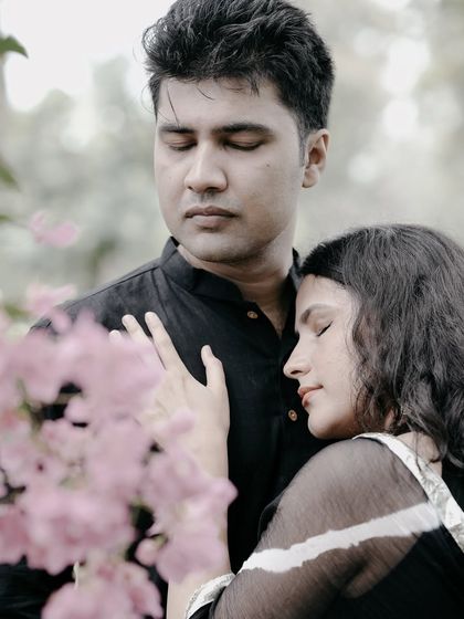A peaceful and intimate moment, with the bride resting her head on the groom's chest, both with eyes closed, framed by flowers.