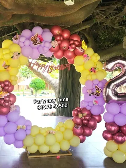 An outdoor butterfly theme for a 2nd birthday. The circular balloon arch with pastel colors looks beautiful against the natural backdrop.