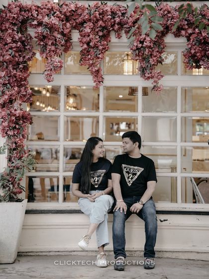 A sweet shot of a couple in matching t-shirts, sitting under a cascade of pink flowers outside a cafe.