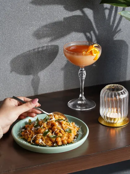 A moody, atmospheric shot of a chickpea dish and a cocktail, using shadows to create a sophisticated and intimate dining vibe.
