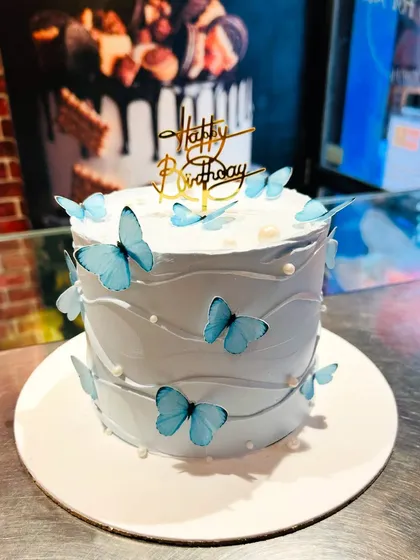A serene light blue cake adorned with delicate blue butterflies and small pearls for a dreamy effect.