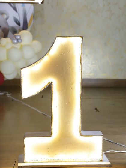 A close-up of a large, brightly lit marquee number '1', a popular add-on for first birthday parties.