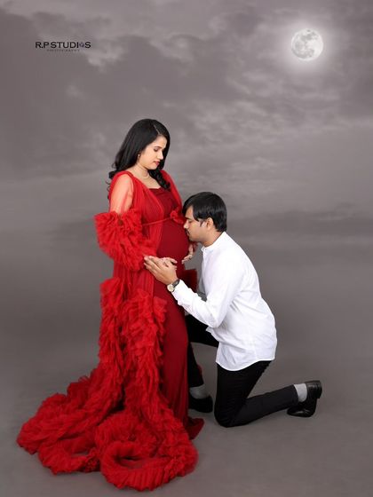 A dramatic and romantic portrait under a painted moon. The flowing red gown and the partner's tender pose create a cinematic and unforgettable image.