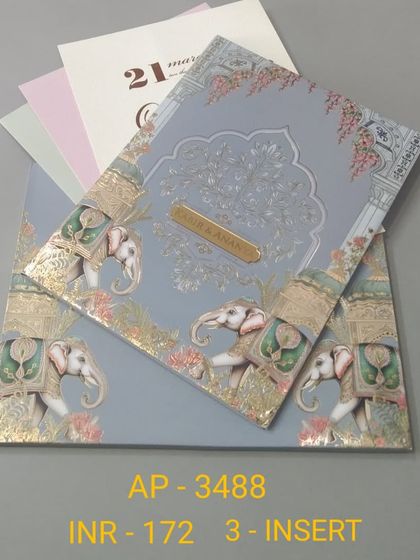 A dusty blue card featuring a border of decorated elephants and a subtle tree of life pattern embossed in the background. This three-insert invitation combines traditional motifs with a gentle color palette.