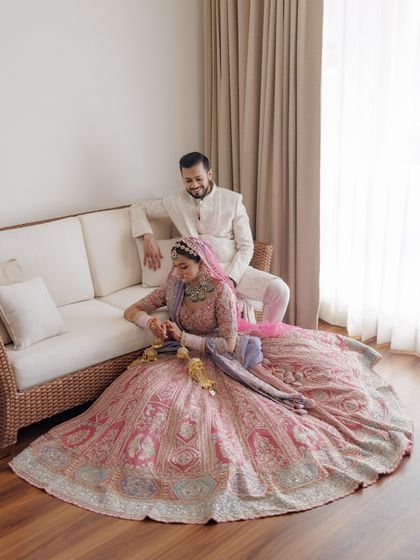 A relaxed portrait of the couple indoors, showcasing the magnificent spread of the bride's lehenga.