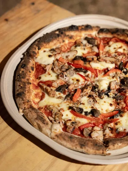 A pizza served on a rustic plate, featuring chicken, mushrooms, and red peppers. This shows one of the many custom combinations we can create for your event.